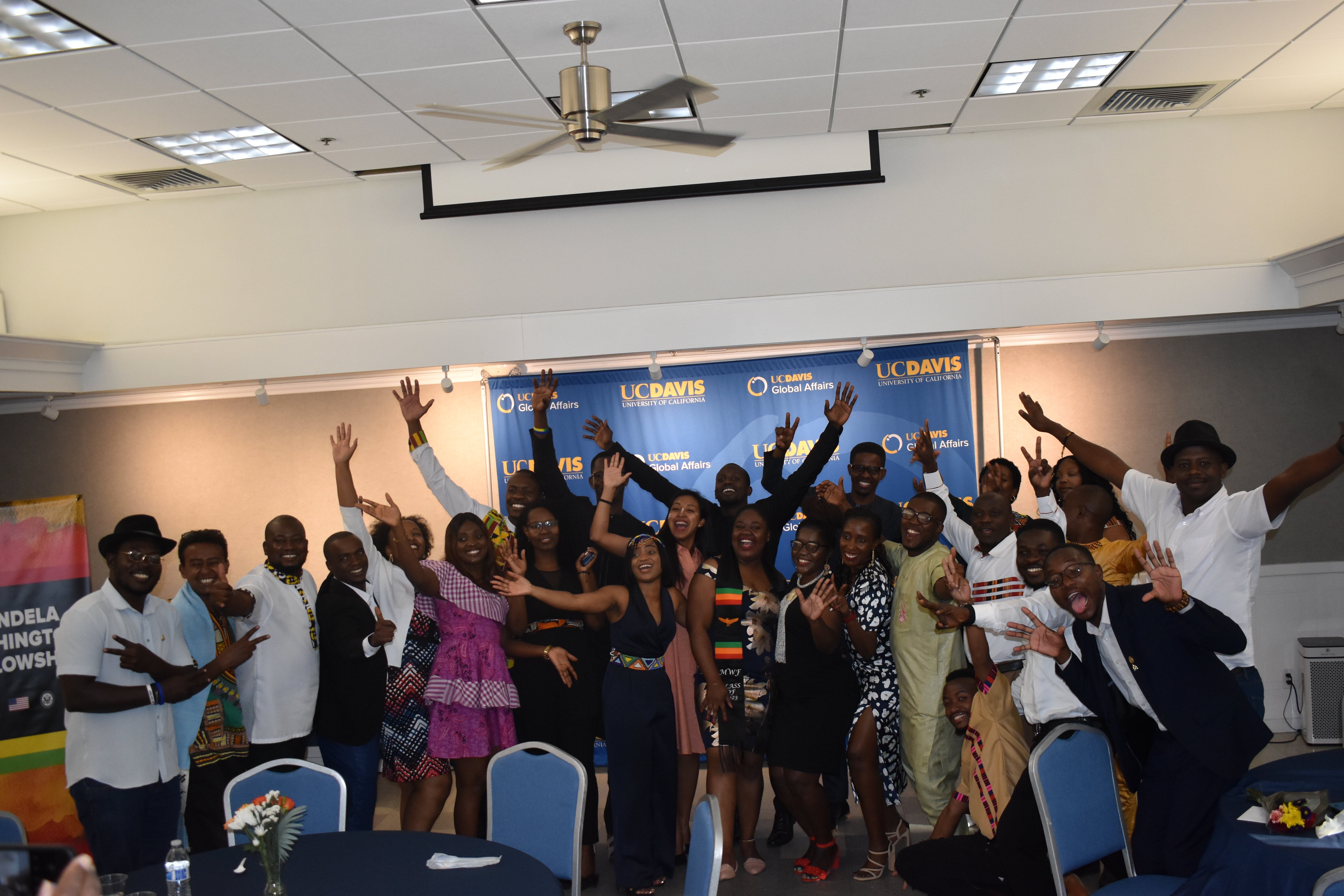The Mandela Washington Fellows smile in front of a UC Davis Global Affairs backdrop with their arms outstretched.