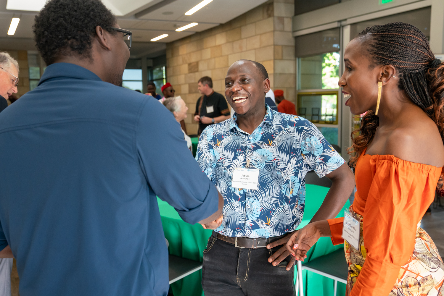 Jabura Muwonge (middle) shakes hands with a man inside the International Center as Angellah Kiiza Kyomugisha smiles to the right.