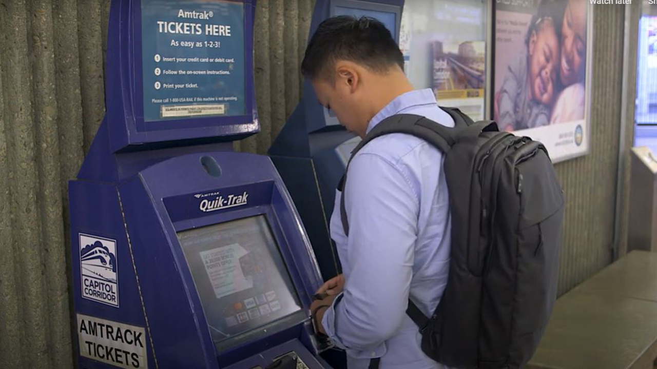 A man stands at a payment kiosk and removes his wallet from his pocket at an Amtrak station.