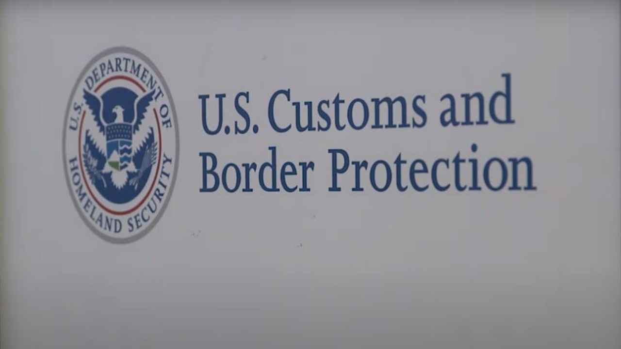 The American government seal for the Department of Homeland Security and the logo for the U.S. Customs and Border Protection printed in blue on a white wall.