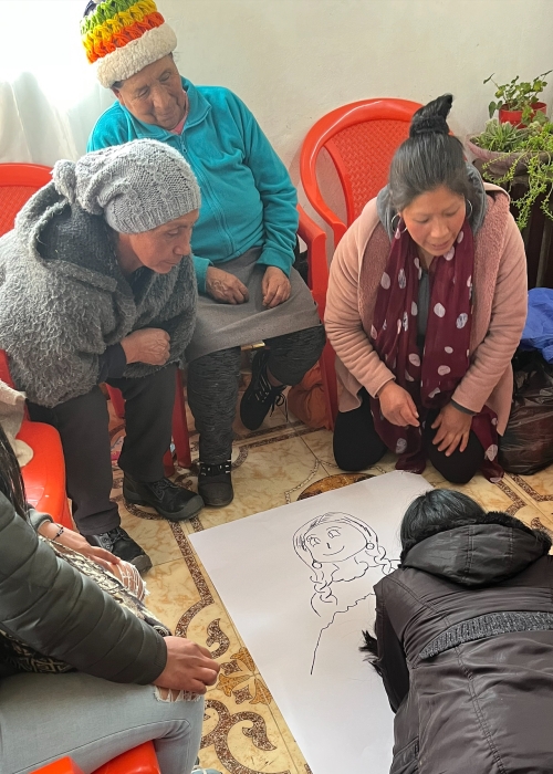 Rural Colombian women are gathered around a drawing of a woman sketched by Professor Raquel Aldana.