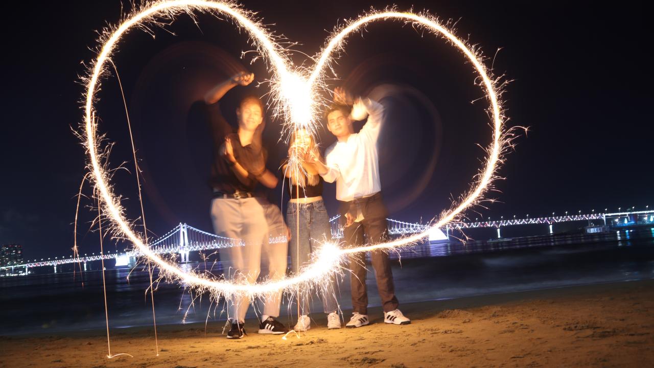 Students on a beach trying to use fireworks to make a heart shape. 
