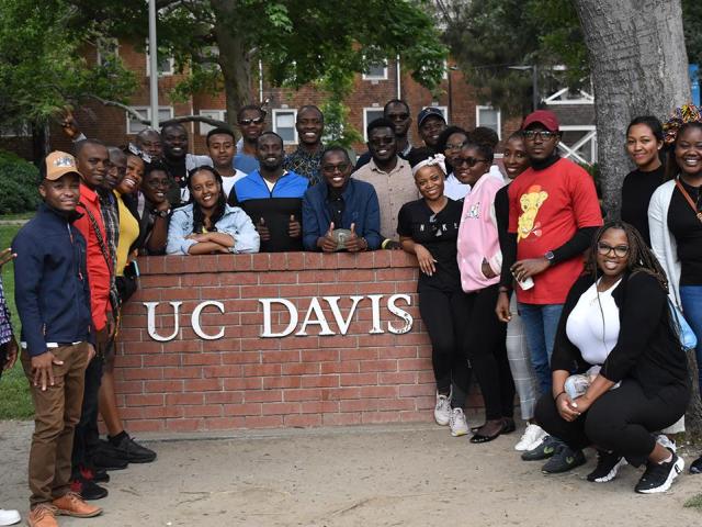 Mandela Washington Fellows stand in front of a UC Davis sign on a brick wall