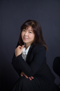 Ya-Ching poses in a black blazer and white button up with a dark background.