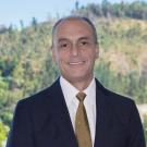 Photo of Mauricio Cañoles in a dark suit and a gold tie smiling at the camera